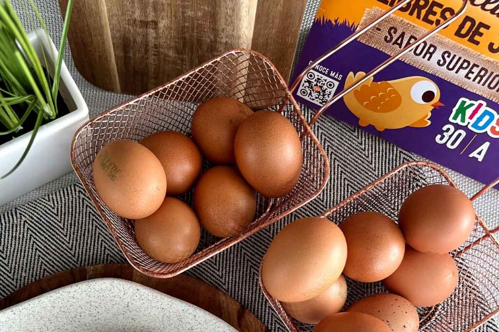Dos pequeñas canastas metálicas de color cobre llenas de huevos rojos sobre un mantel con diseño geométrico