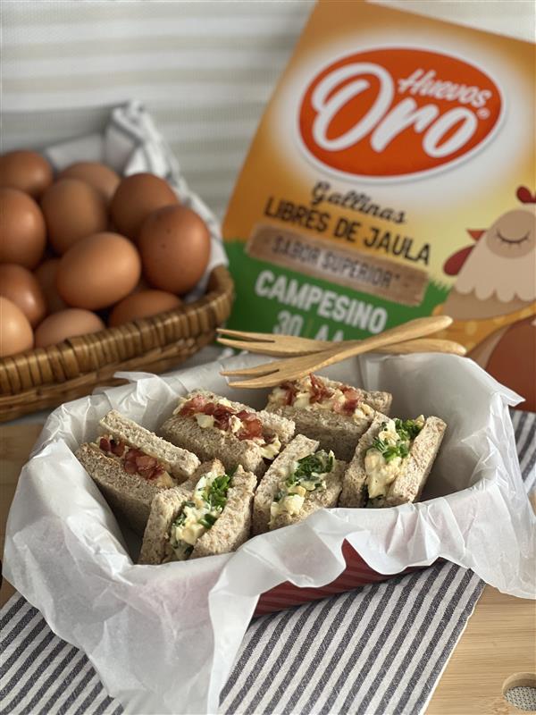 Sándwiches de huevo partidos por la mitad para una cena ligera, acompañados de una caja de Huevos Oro y huevos sueltos.