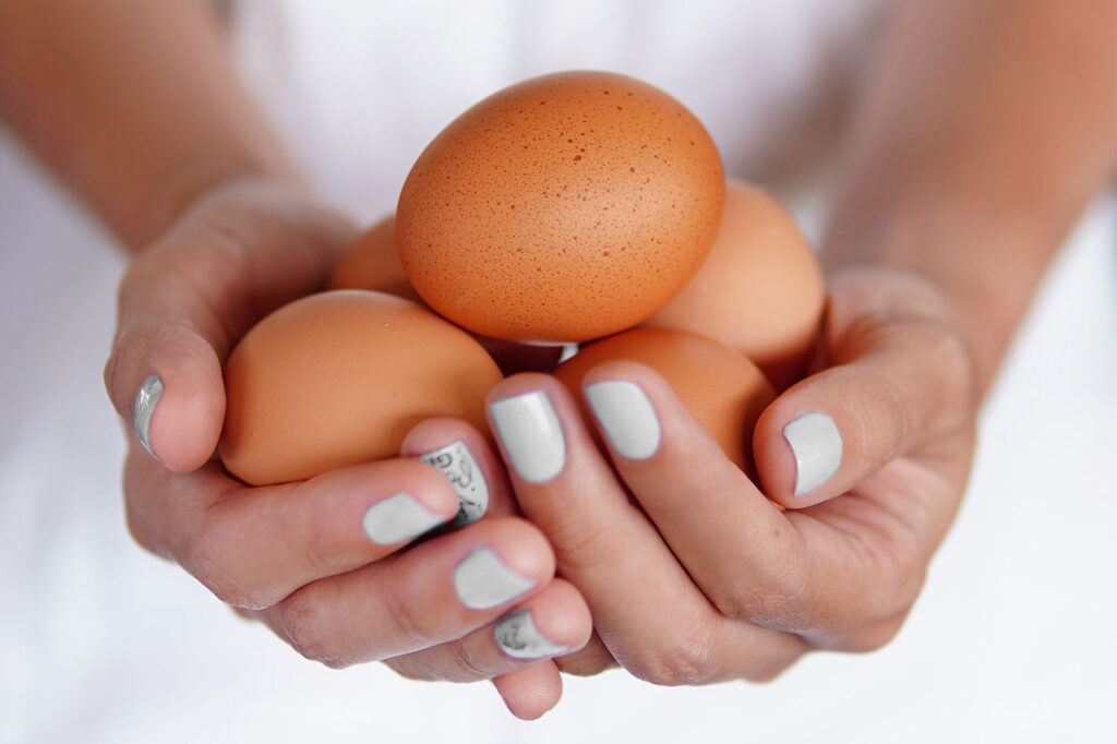 Alguien sosteniendo un puñado de huevos frescos de color marrón entre sus manos.