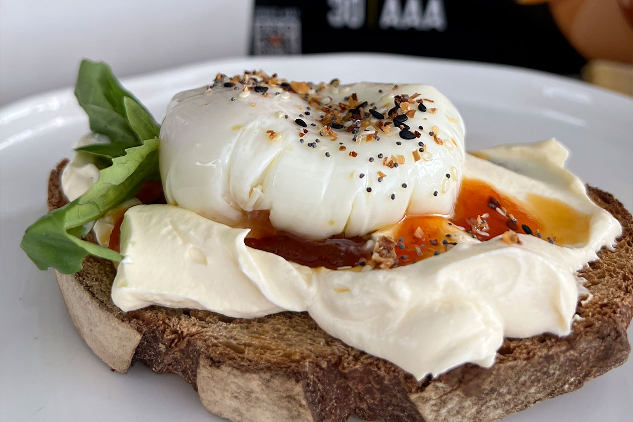 Tostada de pan rústico con crema blanca, un huevo poché encima y especias espolvoreadas.