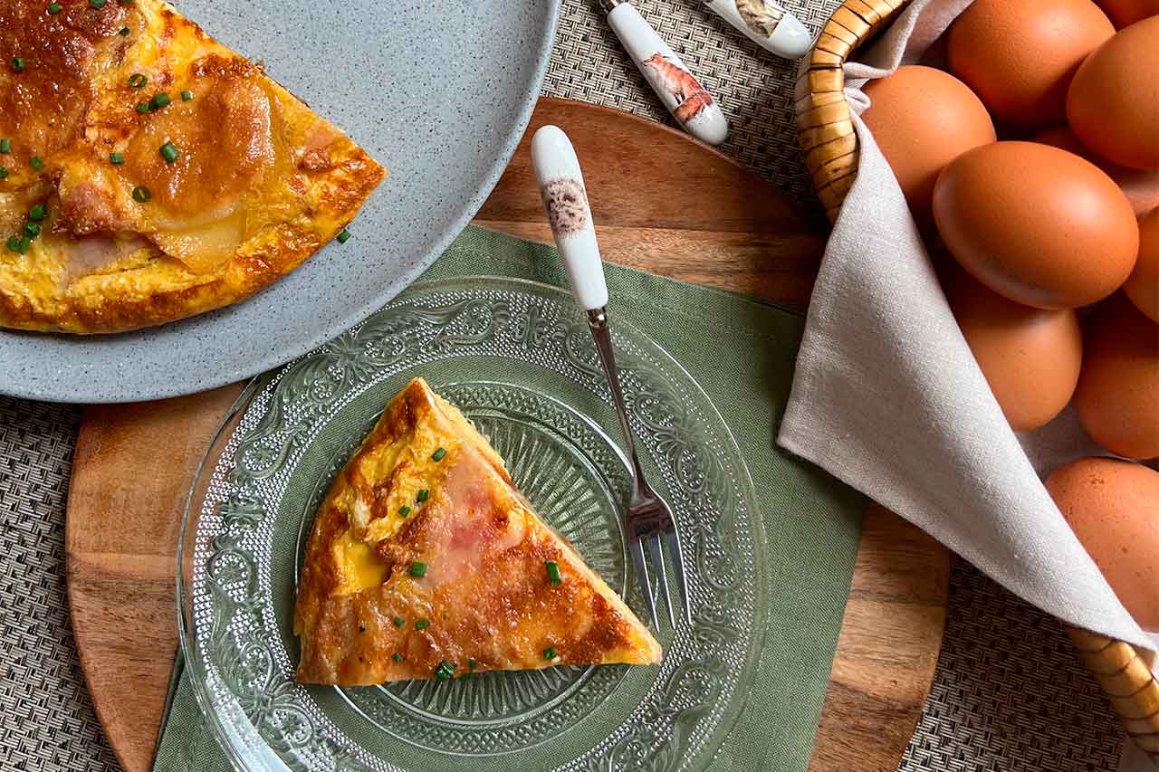 Primer plano de una jugosa porción de tortilla de patatas casera con jamón y cebollino fresco, servida en un plato de cristal