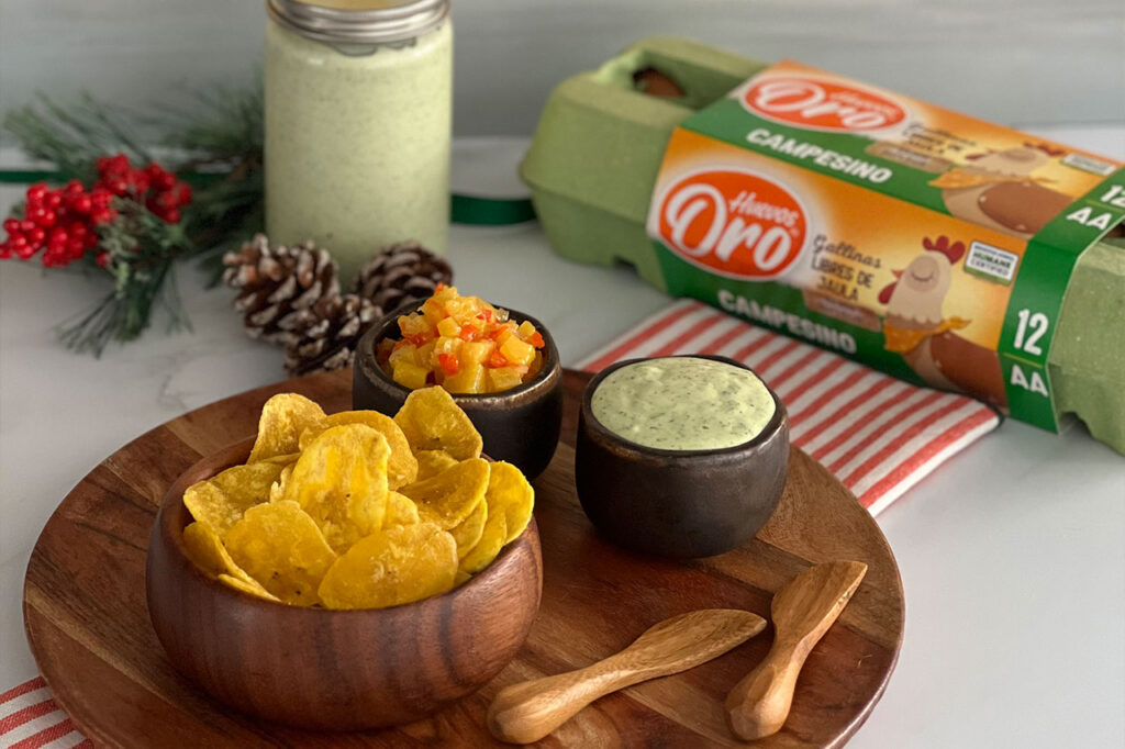 Chips de plátano servidos con salsas caseras a base de huevo. En el fondo, destaca el empaque de "Huevos Oro Campesino"