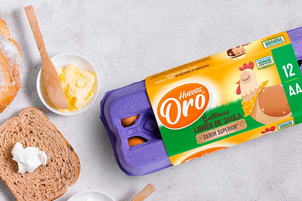 Vista superior de un bodegón de desayuno que incluye un cartón de 12 huevos morado de la marca "Huevos Oro" (gallinas libres de jaula)