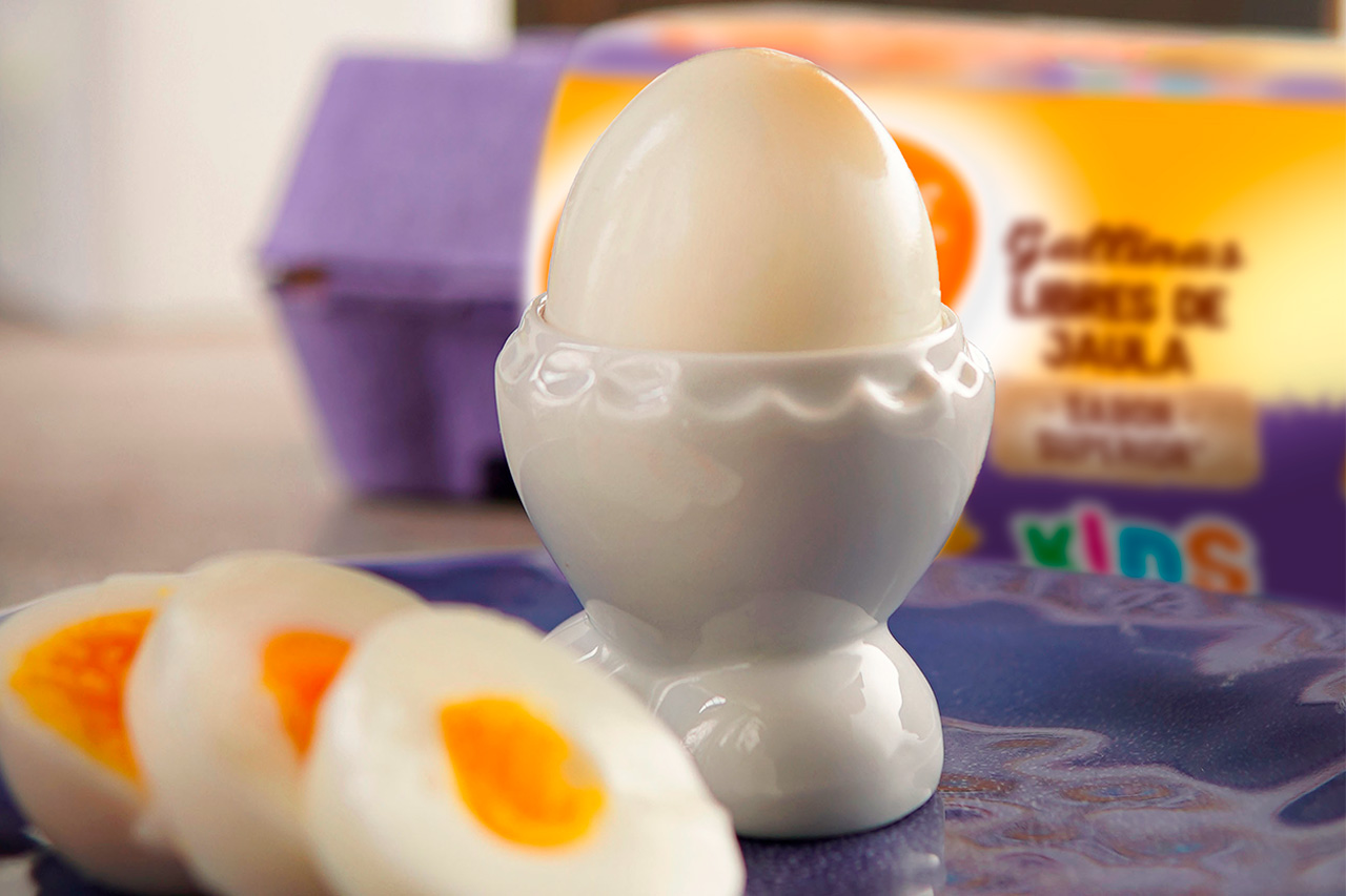 Huevo tibio pelado en una huevera blanca, acompañado de rodajas con yema líquida sobre un plato azul.