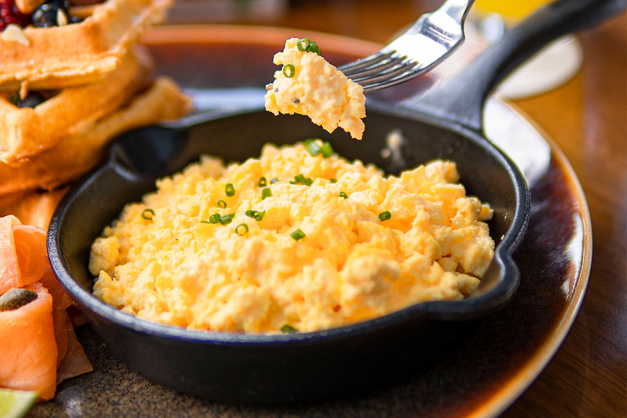 Un pequeño sartén de hierro fundido lleno de huevos revueltos esponjosos, decorados con cebollino fresco picado