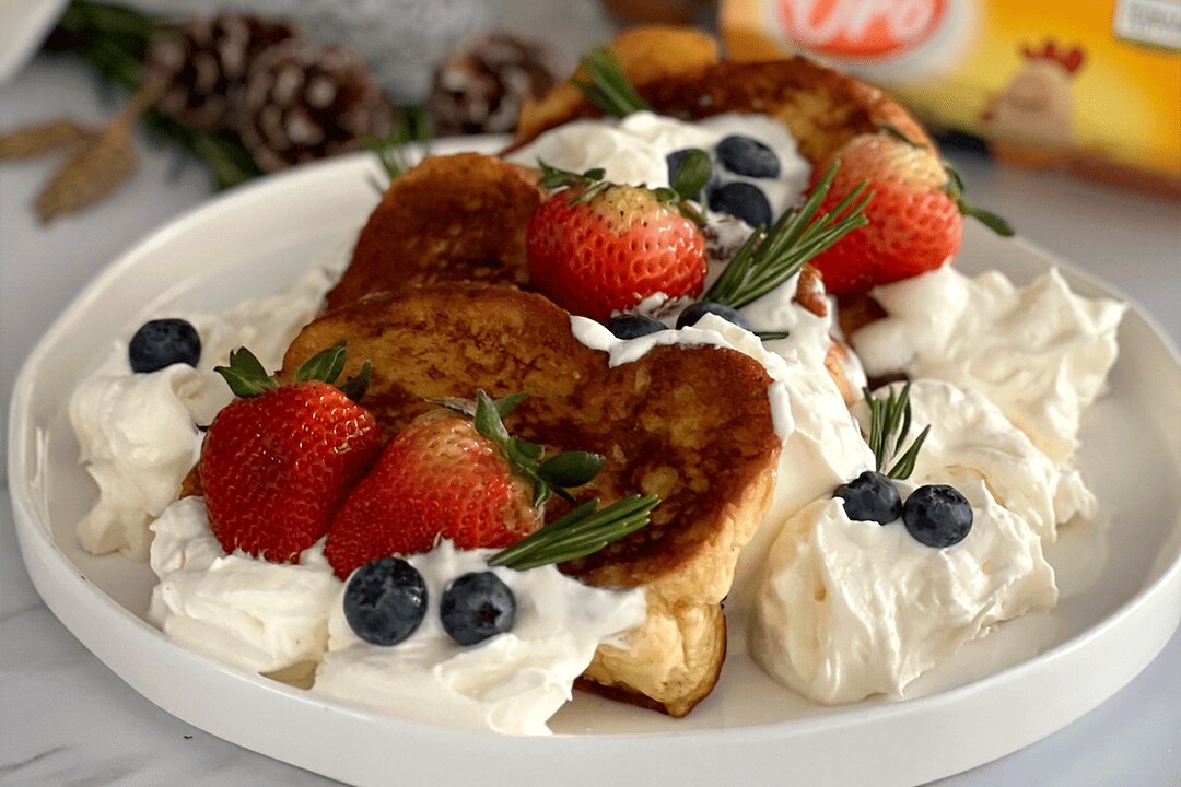 Receta de tostadas francesas caseras con crema batida, fresas frescas y arándanos en un plato blanco.