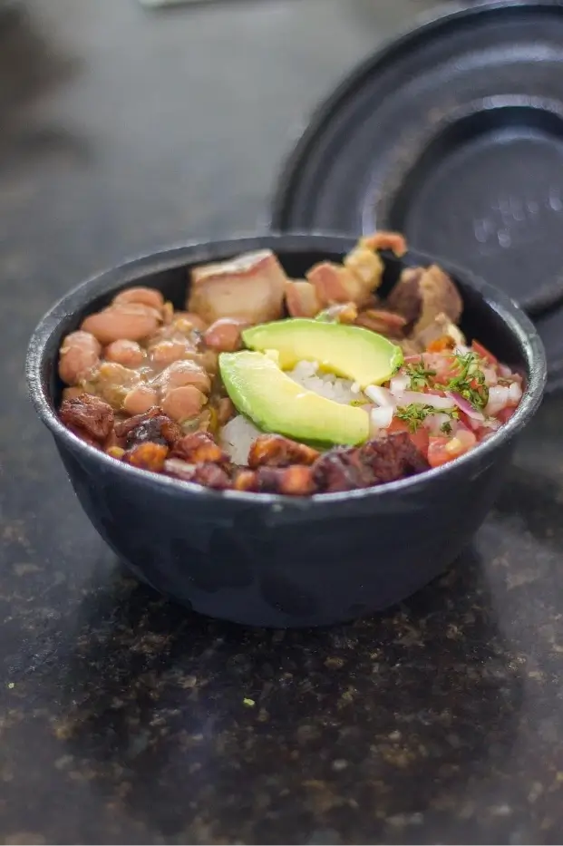 Una cazuela que reúne los ingredientes de una bandeja paisa. 