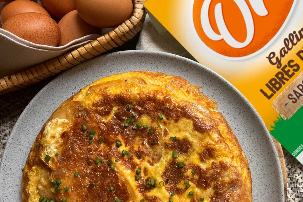 Tortilla española o de patata de forma circular, con una costra exterior dorada y un interior que se percibe jugoso, decorada con cebollino fresco picado.
