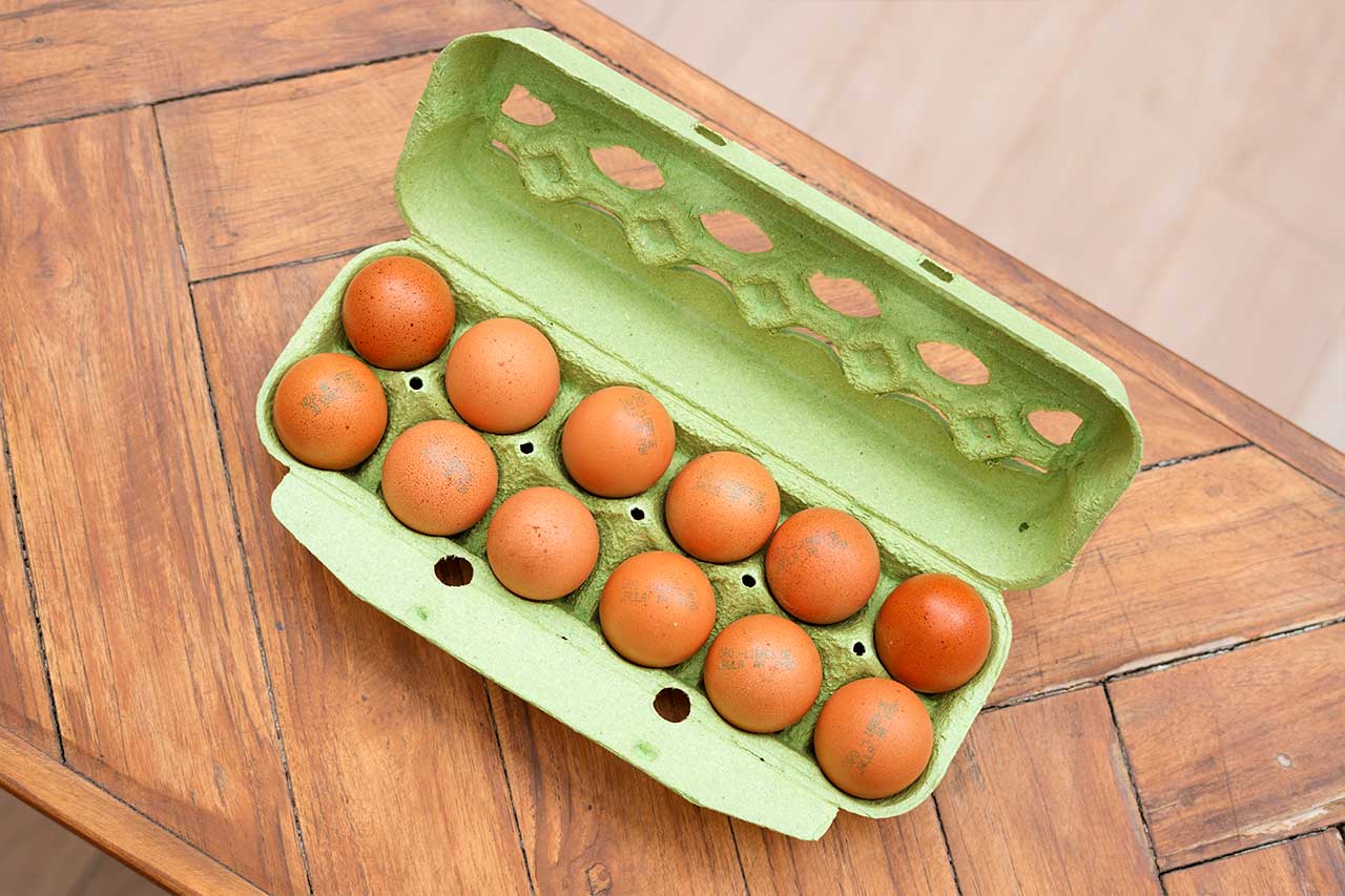 Vista superior de una docena de huevos marrones dentro de un cartón de color verde claro abierto, colocado sobre una mesa de madera rústica